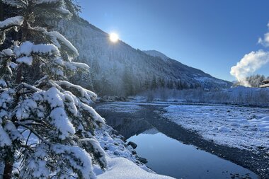 Verschneite Winterlandschaft entlang eines Flusses am Winterwanderweg Garsella im Großen Walsertal bei Sonnenschein. | © Silvia Plangg