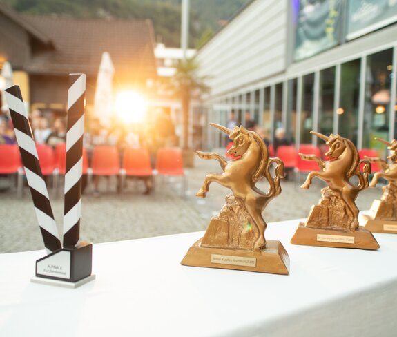 Die Trophäen, das Goldene Einhorn, stehen auf einem Tisch vor den Zuschauerreihen beim Alpinale Kurzfilmfestival bereit. | © Anna Salcher