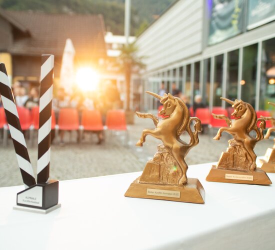 Die Trophäen, das Goldene Einhorn, stehen auf einem Tisch vor den Zuschauerreihen beim Alpinale Kurzfilmfestival bereit. | © Anna Salcher