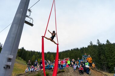 Vertikaltuchkünstlerin schwebt über Publikum auf dem Wanderweg. | © Bergbahnen Brandnertal, Bettina Schwarzhans