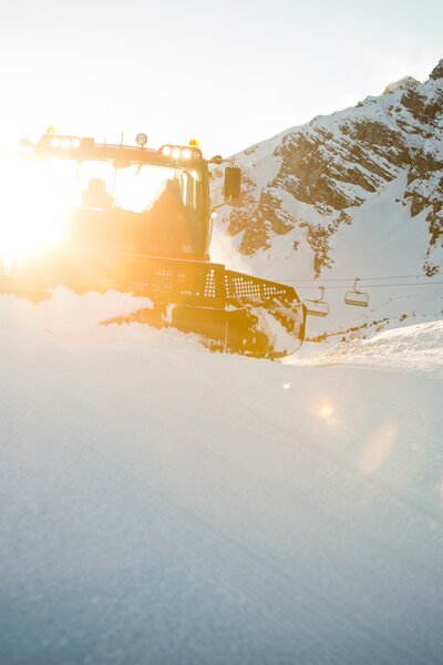Das Gegenlicht strahlt in den PistenBully während die Piste präpariert wird. | © Bergbahnen Brandnertal, Michael Marte
