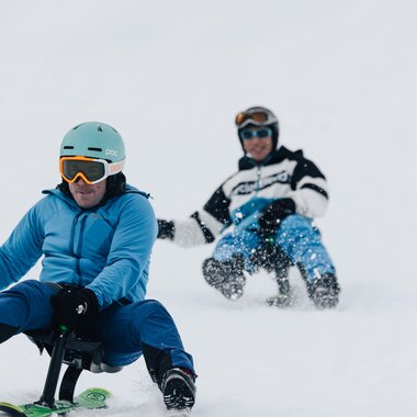 Ein Rodler im Vordergrund rodelt konzentriert auf dem Snooc während ihn ein anderer Rodler verfolgt. | © Bergbahnen Brandnertal, Timo Hummel