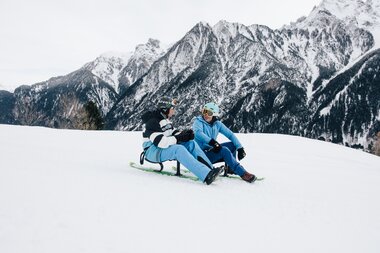 Zwei Herren sitzen auf dem Snooc und reden. Winterlandschaft im Hintergrund. | © Bergbahnen Brandnertal, Timo Hummel